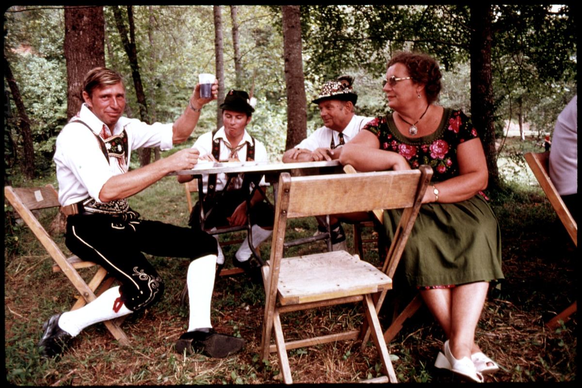 Visitors in Bavarian dress raising glasses at an outdoor table during Helen's 1975 Oktoberfest