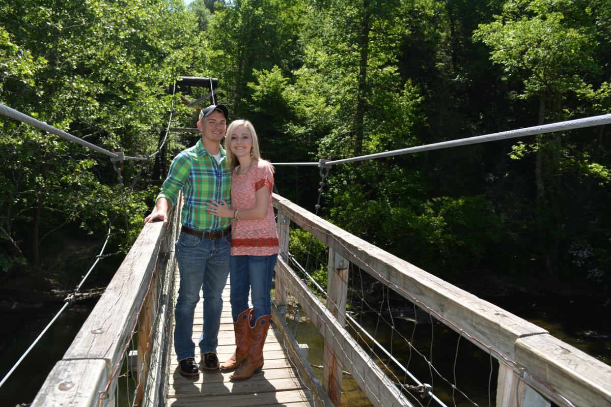 Two hikers standing on the Toccoa River Swinging Bridge surrounded by green forest